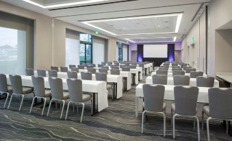 a large conference room with rows of tables and chairs , a projector screen at the front , and two blue and white lights on the ceiling at Hyatt Regency San Francisco Airport