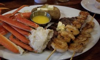 a plate filled with a variety of seafood , including shrimp , crab legs , and steak , accompanied by a side of potatoes at RiverBend Lodge