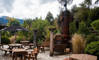 an outdoor dining area with a barbecue grill and several wooden benches surrounding it , creating a cozy atmosphere at Wonderland Makarora Lodge
