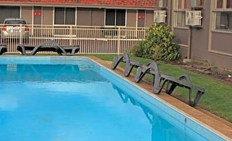 a swimming pool with lounge chairs and umbrellas , surrounded by a building with red - tiled roofs at Hospitality Esperance, SureStay Collection by Best Western