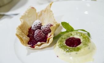a white plate with a dessert made of pastry and fruit , accompanied by a mint leaf at Hotel Alpino