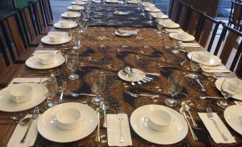 a long dining table is set with white plates , wine glasses , and silverware on a brown and gold tablecloth at HIG Hotel