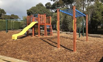 a playground with a slide and monkey bars in a wooded area , surrounded by trees at Prom Coast Holiday Lodge