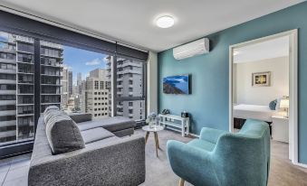 a modern living room with blue and gray furniture , a flat - screen tv , and a large window overlooking the city at Pegasus Apart'Hotel