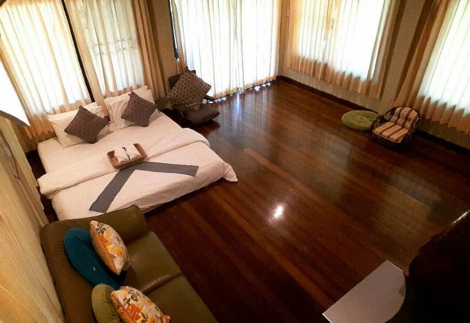 a spacious living room with hardwood floors , large windows , and a comfortable bed in the center at BaanSuanLeelawadee Resort Amphawa