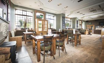 a large , empty restaurant with wooden tables and chairs , surrounded by windows on one side at Columba Hotel Inverness by Compass Hospitality