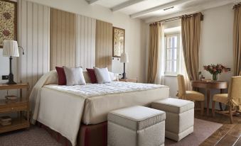 a large bed with white linens and a wooden headboard is in a room with beige walls , lamps , and ottomans at Rosewood Castiglion del Bosco