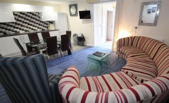 a living room with a striped couch , dining table , chairs , and a tv . also a kitchen in the background at Marine Apartment