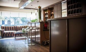 a modern , minimalist bar area with wooden floors and sleek metal furniture , including stools and cabinets at Hotel Carlton