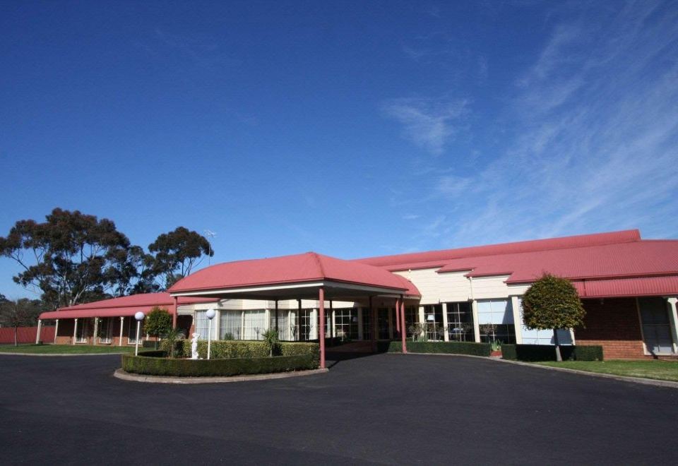 a large building with a red roof and white walls is surrounded by trees and bushes at Grange Burn Motel