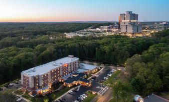 aerial view of a large hotel surrounded by trees , with a parking lot in front of it at Hilton Garden Inn Stony Brook
