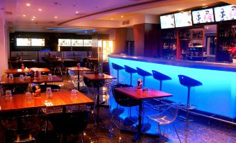 a dimly lit bar with multiple tables and chairs , a blue light display , and television screens at Water's Edge Hotel