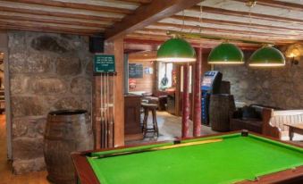 a pool table with a green felt top is in the middle of a room with stone walls and wooden beams at The Commercial Hotel