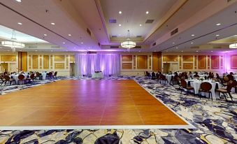 a large , empty banquet hall with a stage and wooden dance floor , illuminated by purple lights at DoubleTree Boston North Shore Danvers