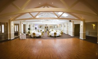 a large , well - lit room with wooden floors and high ceilings , containing multiple round tables set for diners at Best Western Weymouth Hotel Rembrandt