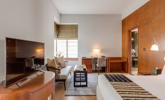 a hotel room with a king - sized bed , a flat - screen tv , and a desk with a laptop at The Manor - New Delhi