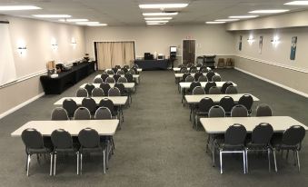a large room with several rows of tables and chairs , a projector screen , and lights on at Thriftlodge Kingston