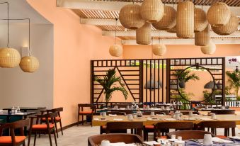 a restaurant with wooden tables and chairs , surrounded by potted plants and hanging lights , set against an orange wall at Salt of Palmar, Mauritius, a Member of Design Hotels