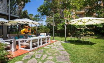 a patio area with a table , chairs , and umbrellas is surrounded by trees and a stone path at Glenferrie Lodge