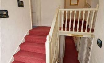 a red carpeted staircase with white railings , leading to the second floor of a house at The White House Guest House