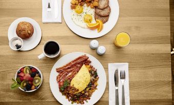 a wooden table is set with various breakfast dishes , including eggs and toast , along with cups of coffee and orange juice at Hilton Garden Inn Boise/Eagle