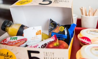 a breakfast tray with various food items , including an apple , bananas , and orange slices , placed in a box at Peartree Lodge Waterside