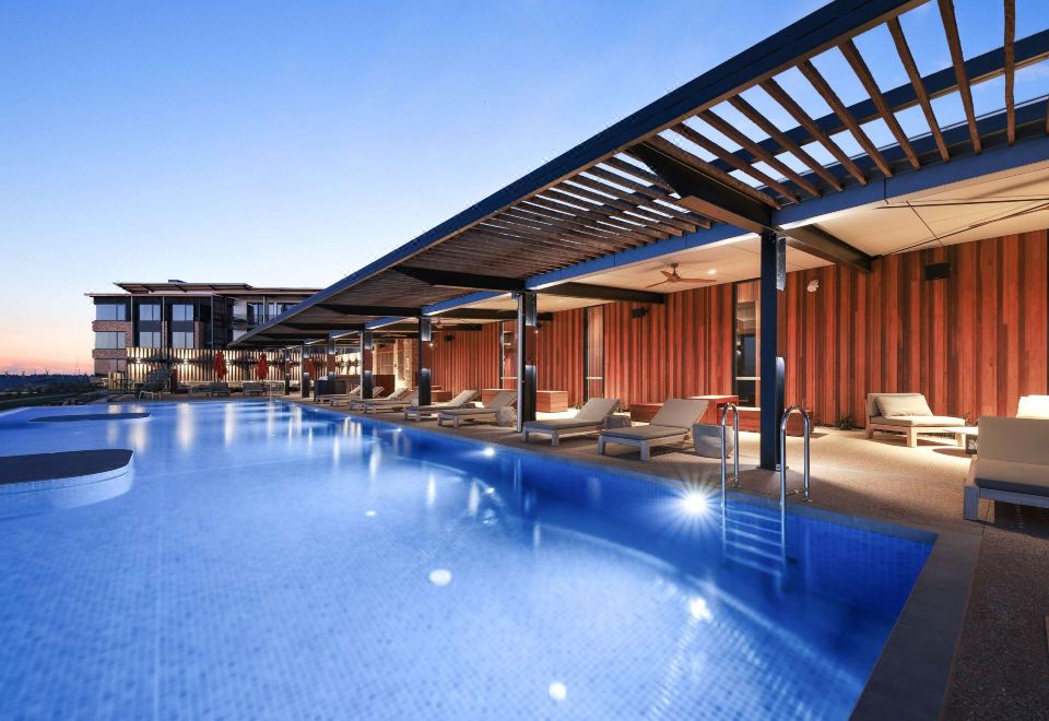 a large swimming pool is surrounded by a wooden structure and lounge chairs in front of it at The Sebel Yarrawonga Silverwoods
