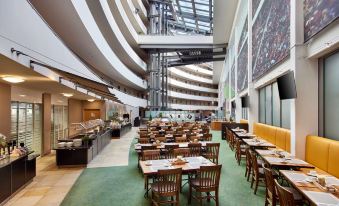 a large , modern cafeteria with multiple dining tables and chairs , surrounded by a high ceiling at Lindner Hotel Leverkusen Bayarena