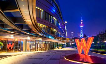 The entrance to a hotel at night is adorned with large windows and a brightly lit sign in front at W Shanghai - The Bund