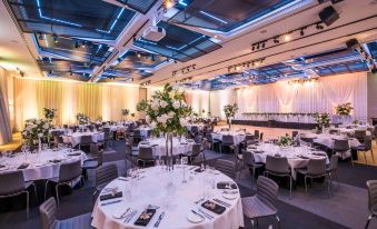 a large banquet hall with round tables and chairs , white tablecloths , and flowers is set up for a formal event at Hyatt Place Melbourne Essendon Fields