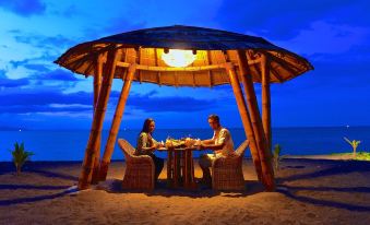 a man and a woman are sitting at a table in a wooden gazebo on the beach at Coconut Garden Beach Resort