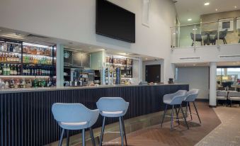 a modern bar with a black countertop , blue chairs , and a television mounted on the wall at DoubleTree by Hilton London Heathrow Airport