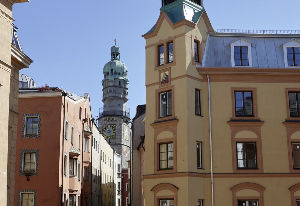 a city street with a tall church steeple in the background , surrounded by various buildings and cars at Hotel Innsbruck