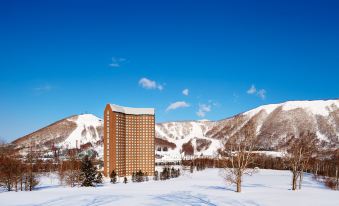 a tall building is surrounded by snow - covered mountains in a snowy landscape with trees and bushes at The Westin Rusutsu Resort