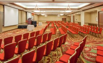 a large conference room with red chairs and a podium , surrounded by white walls and carpet at Sonesta Milwaukee West Wauwatosa