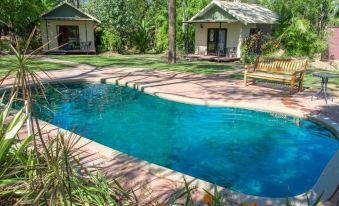 a large swimming pool surrounded by lush green grass and trees , with several lounge chairs placed around the pool area at Breeze Holiday Parks - Mary River