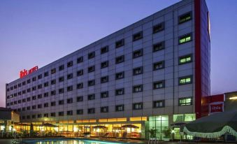 a large hotel building with a swimming pool in front of it at night , illuminated by the setting sun at Ibis Lagos Ikeja