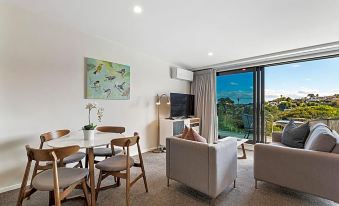 a modern living room with a dining table and chairs , a television , and a view of the ocean at Fernz Motel & Apartments Birkenhead