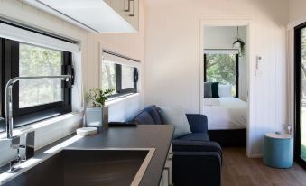 a modern , minimalist living room with a couch and a kitchen counter , connected to a bedroom through an open door at Reflections Jimmys Beach - Holiday Park