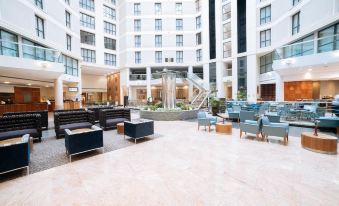 a modern hotel lobby with a large atrium , multiple couches , chairs , and tables , as well as a staircase leading to the second floor at Sofitel London Gatwick