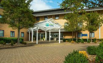 an exterior view of a hotel or motel , featuring a large building with a white canopy over the entrance at Holiday Inn Express Milton Keynes
