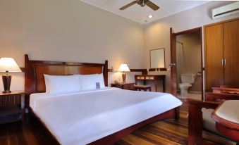 a large bed with white sheets and a wooden headboard is in a room with a desk , chair , and lamp at Berjaya Tioman Resort