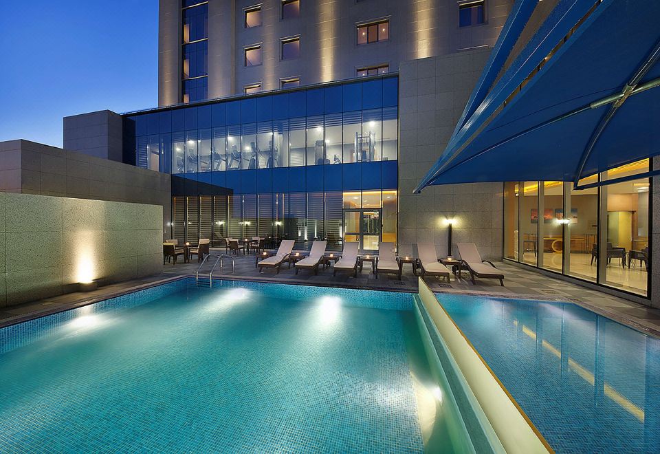 a large swimming pool is surrounded by lounge chairs and a building with a blue facade at Hilton Garden Inn Tabuk