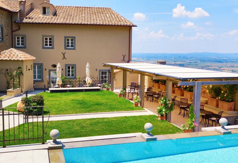 a large villa with a swimming pool and outdoor dining area , surrounded by green grass and trees at Monastero di Cortona Hotel & Spa