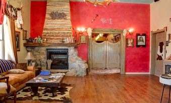a cozy living room with a fireplace , red walls , and wooden floors , featuring a couch , coffee table , and various items on the floor at Tombstone Monument Guest Ranch