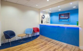 a hotel lobby with a blue reception desk and a seating area , as well as a television at Travelodge Leatherhead