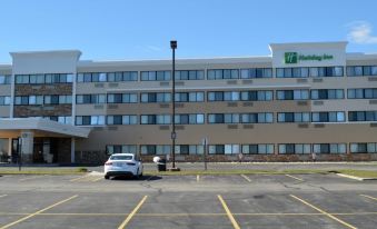 a white car is parked in a lot with a tall building and a parking lot at Holiday Inn Express Big Rapids