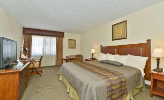 a large bed with a wooden headboard and footboard is in the middle of a room with two chairs , lamps , and framed pictures on at Best Western Prairie Inn  Conference Center