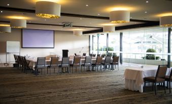 a large conference room with multiple tables and chairs , a projector screen , and multiple hanging lights at The Executive Inn, Newcastle