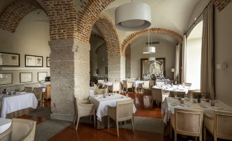 a large dining room with a brick wall and arches , tables set for a meal at Parador de La Granja